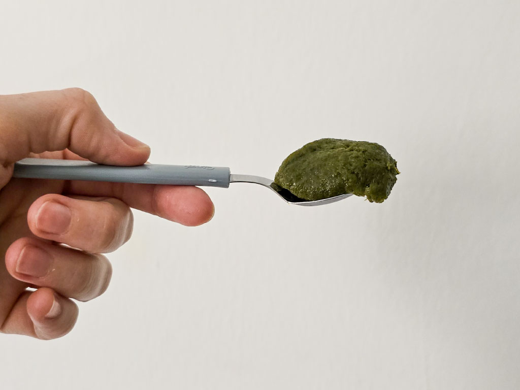 foto de una mano sosteniendo una cuchara con caldito de verduras concentrado apto sibo bajo en fodmaps para cocinar. La vista es lateral y el fondo es blanco