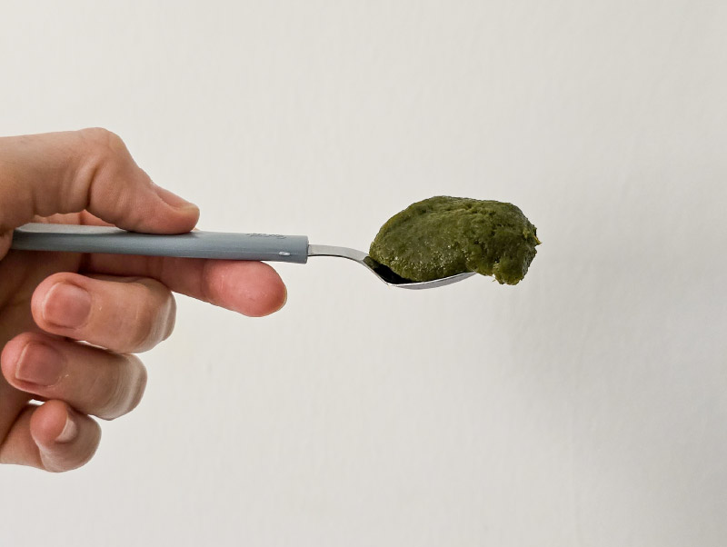 foto de una mano sosteniendo una cuchara con caldito de verduras concentrado apto sibo bajo en fodmaps para cocinar. La vista es lateral y el fondo es blanco